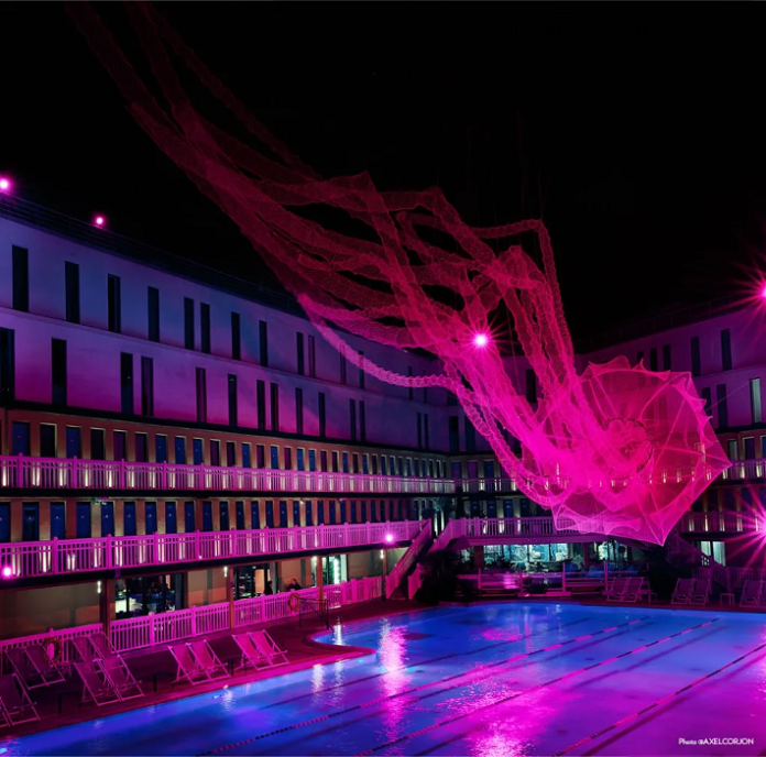 Amic hat bei einem Projekt teilgenommen, bei dem eine 25 Meter lange neonpinke Qualle über dem Molitor-Schwimmbad in Paris schwebt. Quelle: Amic